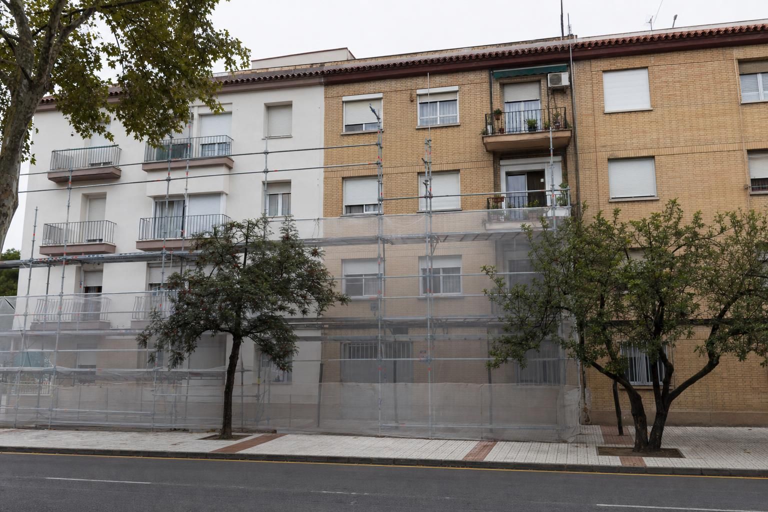 Fachada de un bloque de viviendas de los años 70 con andamio y malla durante una rehabilitación energética